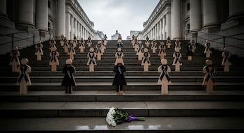 Escalera de un edificio clásico con decenas de figuras de madera femeninas y lazos negros. Un ramo de flores blancas yace en el primer escalón.
