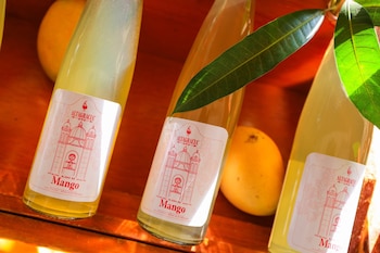 Primer plano de tres botellas de vino artesanal de mango Altagracia sobre una superficie de madera, con mangos frescos y hojas verdes alrededor