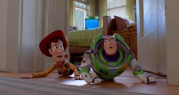 Dos figuras de acción, Woody con sombrero y Buzz Lightyear, se tienden en el suelo de madera. Se observa una cama y una ventana al fondo de una habitación