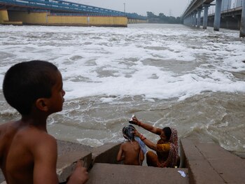 Una mujer baña a su hijo en las orillas del río Yamuna parcialmente cubierto de espuma, en Nueva Delhi, India, el 2 de septiembre de 2024. REUTERS/Priyanshu Singh