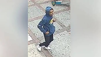Un individuo viste una sudadera azul con capucha, pantalones oscuros y calzado blanco mientras camina sobre un suelo con baldosas