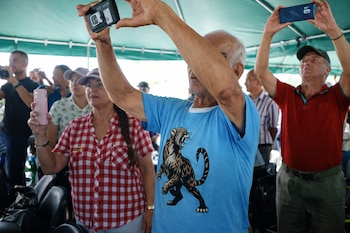 Un hombre con camiseta azul, otro con camiseta roja y una mujer con camisa a cuadros sostienen teléfonos celulares en alto bajo una carpa verde.