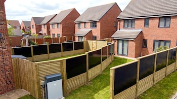 Casas de ladrillo con jardines, vallas de madera y paneles solares negros integrados, además de una unidad exterior de almacenamiento de energía.