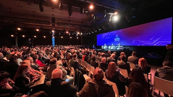Gran audiencia en un auditorio oscuro, tres oradores sentados en un escenario frente a una pantalla con el logo COPEC, y luces de ambiente en el techo