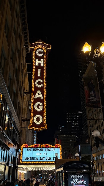 Cartel vertical iluminado del Teatro Chicago en la noche. La marquesina con luces de neón anuncia shows. Edificios oscuros y farolas de la ciudad visibles