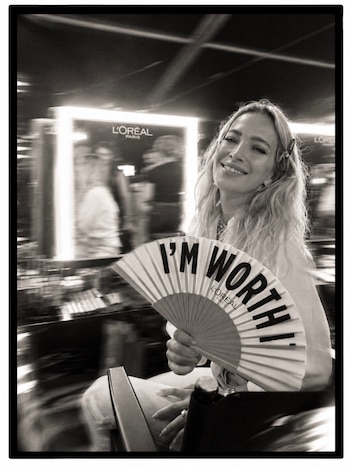 Fotografía en blanco y negro de una mujer sonriendo con un abanico desplegado frente a un espejo iluminado
