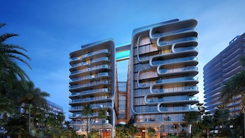 Edificio One Thousand Museum en Miami, un rascacielos moderno con balcones curvos y una piscina elevada. Rodeado de palmeras bajo un cielo azul oscuro