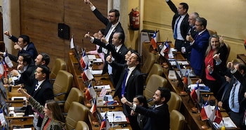 Vista aérea de legisladores chilenos, hombres y mujeres, en un hemiciclo. Varios levantan el pulgar; hay banderas chilenas sobre los escritorios