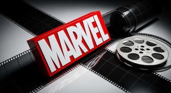 Logo Marvel tridimensional rojo y blanco sobre tira de película cinematográfica desenrollada, con rollo de cine y otra tira enrollada en una superficie reflectante.