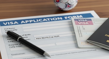 Una solicitud de visado para la Copa Mundial FIFA 2026 con un campo rellenado, una pluma negra, un pasaporte abierto y un balón de fútbol al fondo sobre una mesa de madera.