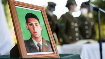 Primer plano de un retrato fotográfico enmarcado de un joven carabinero con uniforme verde sobre una mesa, con figuras uniformadas borrosas al fondo