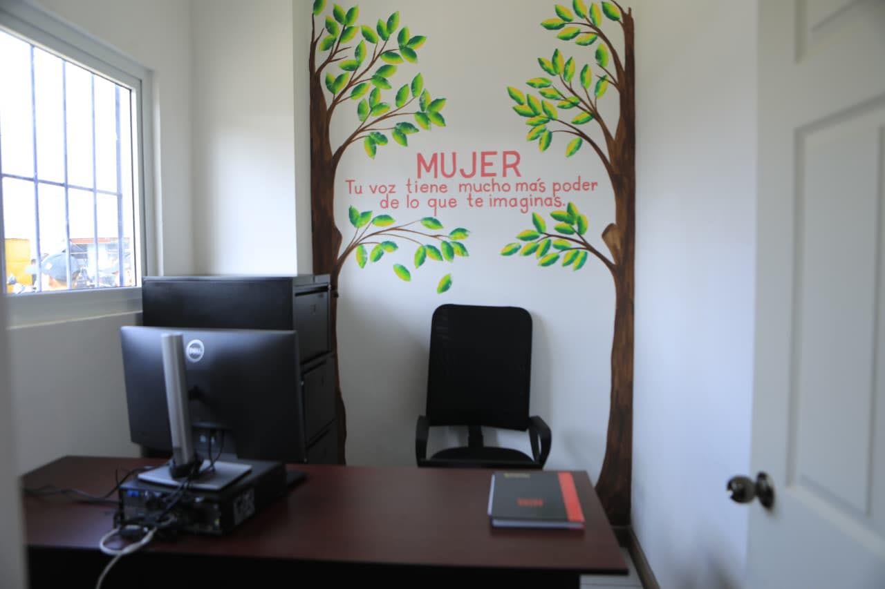 Una oficina luminosa con un escritorio de computadora, una silla de oficina y un mural con el mensaje