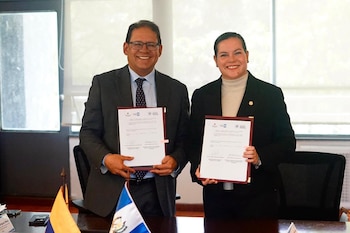Un hombre y una mujer sonríen y sostienen dos documentos firmados. En la mesa hay dos banderas, una de Ecuador y otra de Guatemala
