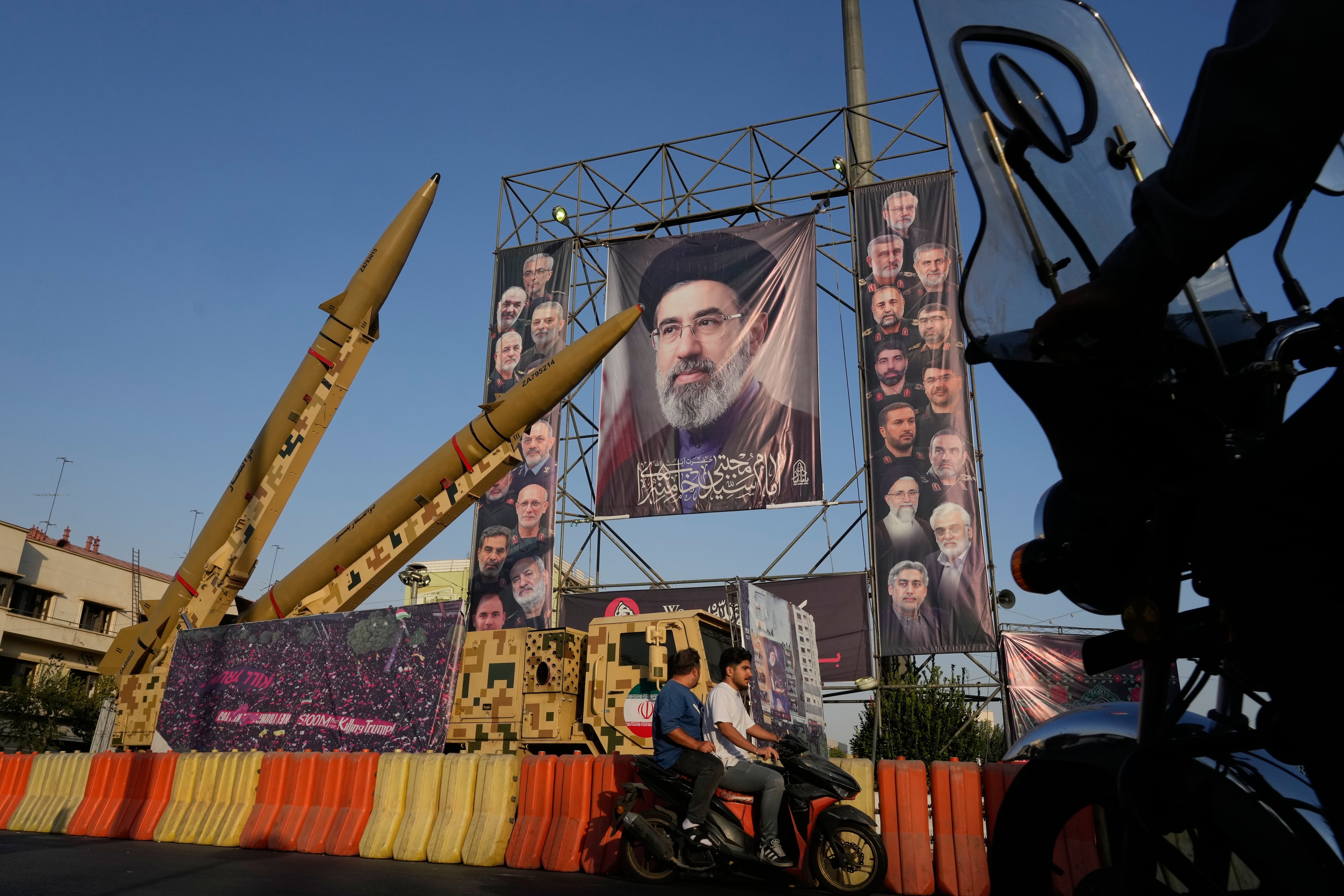 Motocicletas pasan junto a misiles y carteles iraníes con la imagen del líder supremo, el ayatollh Mojtaba Khamenei, en Teherán (AP Foto/Vahid Salemi)