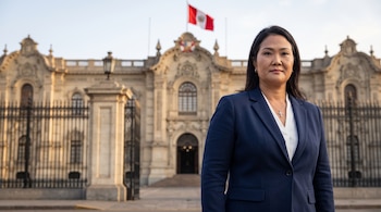 Keiko Fujimori, mujer de cabello oscuro y traje azul, de pie frente al Palacio de Gobierno de Perú, que tiene una bandera peruana en la parte superior.