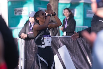 Una atleta con uniforme negro y dorsal número 11 junta las manos frente al rostro ante vallas de seguridad y público