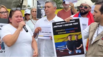 Una mujer llorando habla por un micrófono en una manifestación, flanqueada por personas con pancartas pidiendo la libertad de Jonathan y Cristian Tisoy