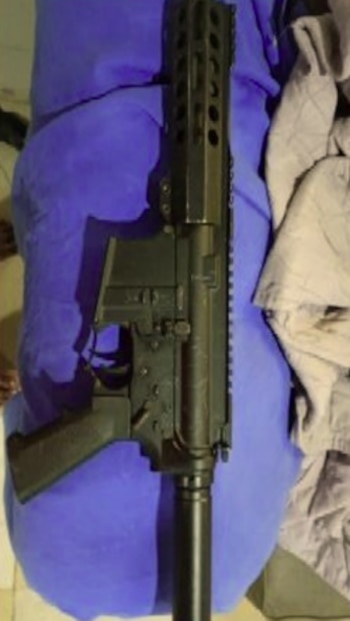Un fusil de color negro colocado sobre una manta azul junto a ropa de cama clara