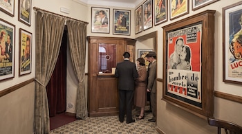 Personas ante una taquilla de madera en el vestíbulo de un cine con carteles de películas en las paredes y cortinas en la puerta.