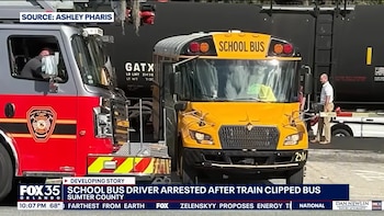 Un autobús escolar amarillo está estacionado junto a un camión de bomberos rojo y gris y un vagón de tren negro. Se ve personal de emergencia