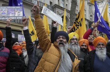 Un grupo de manifestantes sijes con turbantes y barbas, algunos levantando brazos y pancartas, y banderas amarillas y azules al fondo