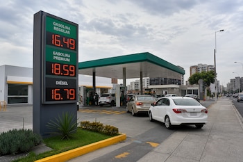 Cartel con cifras digitales de precios de combustible, surtidores y automóviles en el patio de una gasolinera.