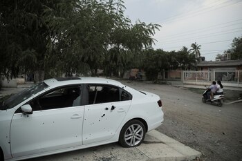 People drive a motorcycle past a car with bullet impacts near the scene where vigilante leader Hipolito Mora was killed, along his bodyguards, during an attack by unknown assailants, in the town of Felipe Carrillo Puerto, in Michoacan state, Mexico June 29, 2023. REUTERS/Ivan Arias