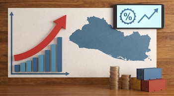 Vista aérea de un gráfico de barras ascendente, un mapa de El Salvador, un teléfono con datos económicos, pilas de monedas y contenedores de envío en una mesa de madera.