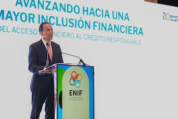 Hombre de traje hablando ante un podio con micrófono. Detrás, una pantalla grande con texto sobre inclusión financiera y el logotipo ENIF y Banco de Guatemala
