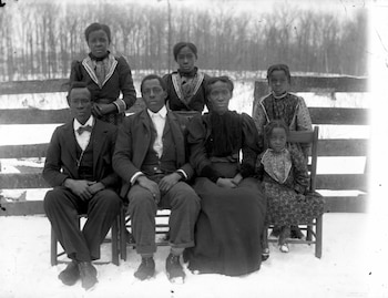 Una fotografía en blanco y negro de siete personas afroamericanas, dos hombres sentados, tres mujeres adultas y dos niñas. Hay nieve en el suelo y una cerca de madera al fondo