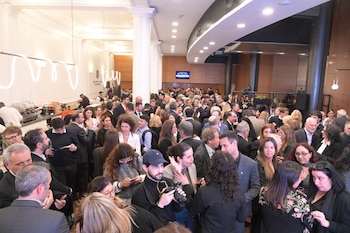 Personas reunidas alrededor de mesas con bocadillos en un salón con el emblema del Colegio Público de la Abogacía de la Capital Federal