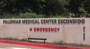 Un cartel de concreto muestra el texto "PALOMAR MEDICAL CENTER ESCONDIDO" y "EMERGENCY" en rojo con una cruz, rodeado de vegetación