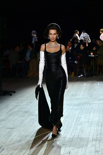 Bella Hadid también estuvo presente en el fashion show del diseñador siendo una de las grandes estrellas. Un espléndido vestido negro de paillettes con escote rectangular, guantes blancos 3/4 stilettos y joyas de brillantes