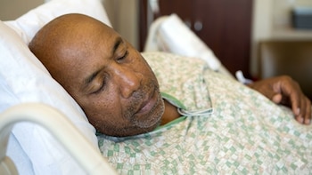 Primer plano de un hombre afroamericano de mediana edad durmiendo profundamente en una cama de hospital, vistiendo una bata estampada
