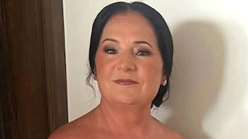 Retrato de una mujer de mediana edad con cabello oscuro peinado hacia atrás, maquillaje sutil y aretes, mirando directamente a la cámara