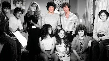 Fotografía de un grupo diverso de diez personas, entre adultos y niños, donde dos hombres de pie al fondo aparecen a color, el resto en blanco y negro.