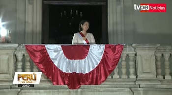 Mujer con banda presidencial en un balcón decorado con telas rojas y blancas. Al fondo, una entrada oscura. Arriba a la derecha, logotipo de TVPerú Noticias