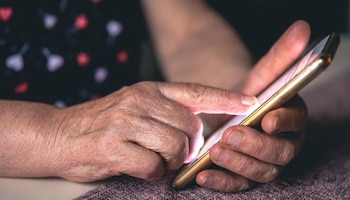 Primer plano de dos manos que sostienen y tocan la pantalla táctil iluminada de un teléfono móvil sobre una superficie oscura