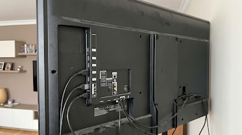 Parte trasera de un televisor negro con múltiples puertos de conexión, incluyendo USB y HDMI, con cables enchufados y algo de polvo.
