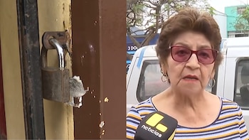 Un candado metálico roto en una puerta de madera, y una mujer con cabello castaño y gafas rojas hablando a un micrófono con el logo de "noticias"
