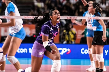 Una jugadora de voleibol con uniforme morado festeja con el puño cerrado cerca de la red frente a otras deportistas en la cancha