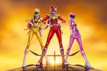 Tres figuras vestidas como Power Rangers de color amarillo, rojo y rosa posan ante un fondo anaranjado iluminado