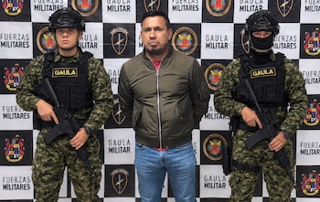 Efectivos policiales uniformados custodian a civiles junto a una mesa con frascos rojos, teléfonos móviles y equipos portátiles