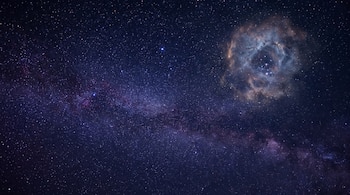 Fondo oscuro con múltiples estrellas y una nebulosa circular de tonos marrones y azulados en la parte superior derecha.