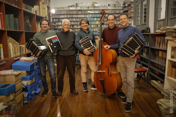 Fotografía en blanco y negro de cuatro músicos sentados en círculo con bandoneones. Un hombre mayor gesticula mientras tres personas más jóvenes los sostienen