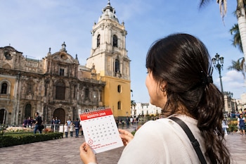 Una persona sostiene un calendario de mesa que marca el 30 de agosto, con una catedral histórica en el fondo