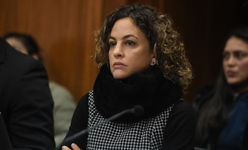 Primer plano de una mujer de cabello rizado castaño, aretes, bufanda negra de textura suave y blusa con patrón de cuadros pequeños
