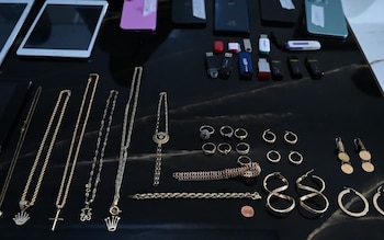 Vista aérea de una superficie oscura que muestra varios teléfonos, tabletas, unidades USB, y una variedad de joyas como anillos, collares y pulseras