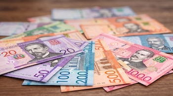 Billetes de peso dominicano de 20, 50, 100, 200, 500 y 1000 pesos esparcidos sobre una mesa de madera.