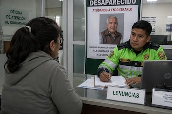 Un policía escribe en un formulario frente a una mujer en un escritorio con un cartel de una persona desaparecida detrás